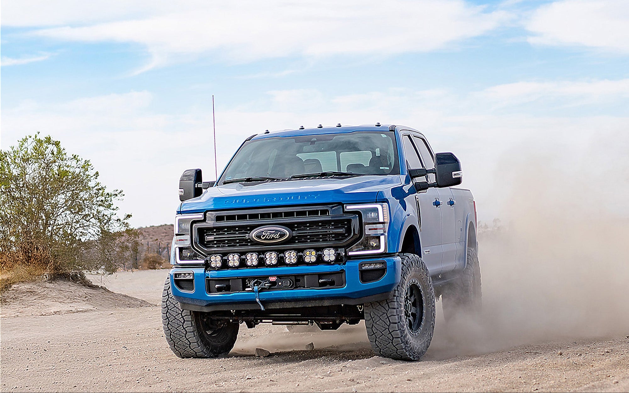 Blue Ford truck driving on a dirt road with a clear sky.