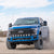Blue Ford truck driving on a dirt road with a clear sky.