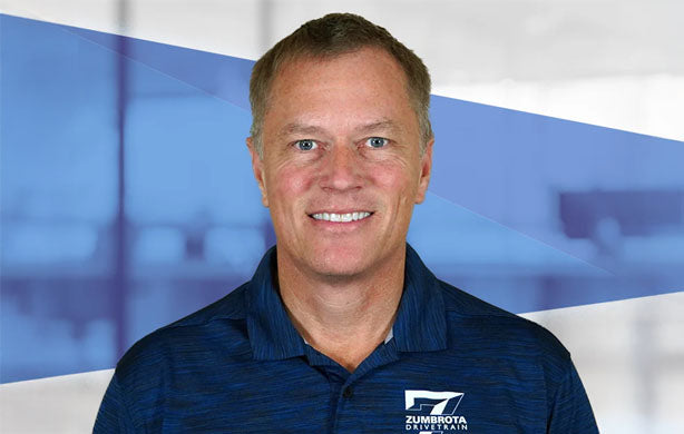 Man wearing a blue shirt with a logo in front of a blurred indoor background